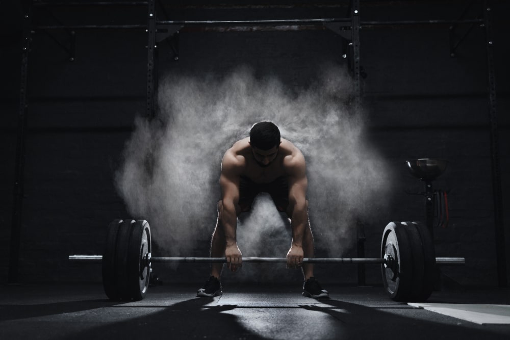 Crossfit athlete prepares to lift heavy barbell in a cloud of dust in the gym
