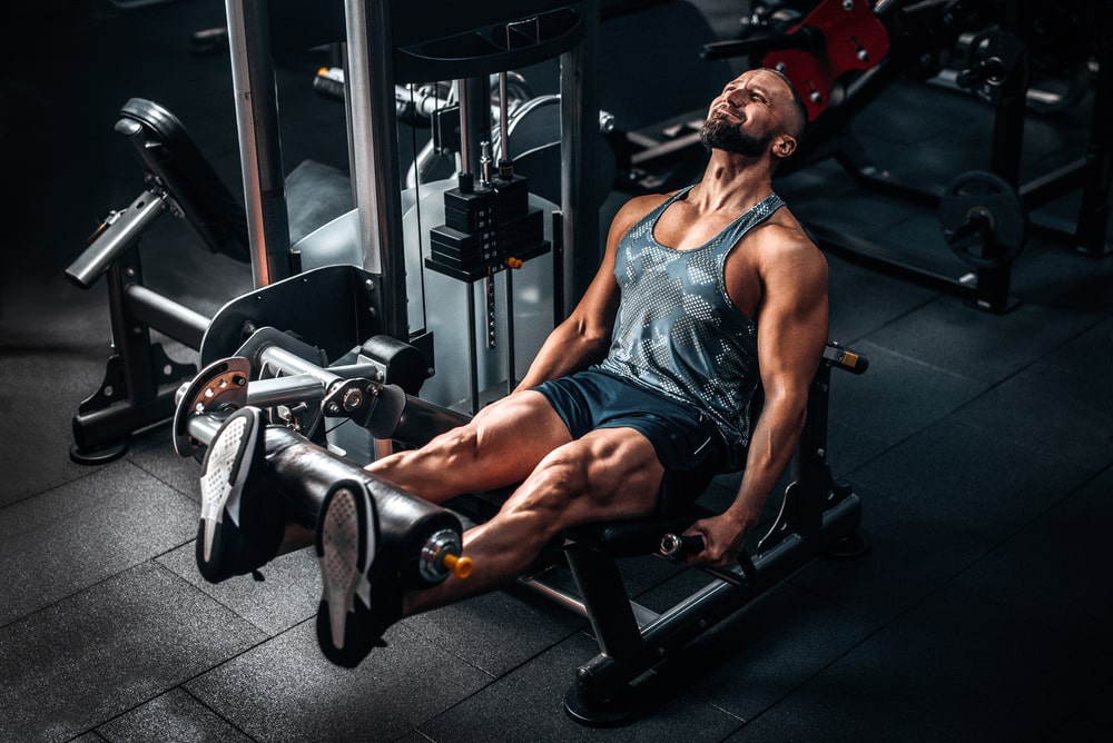 Muscular man using weights machine for legs at the gym