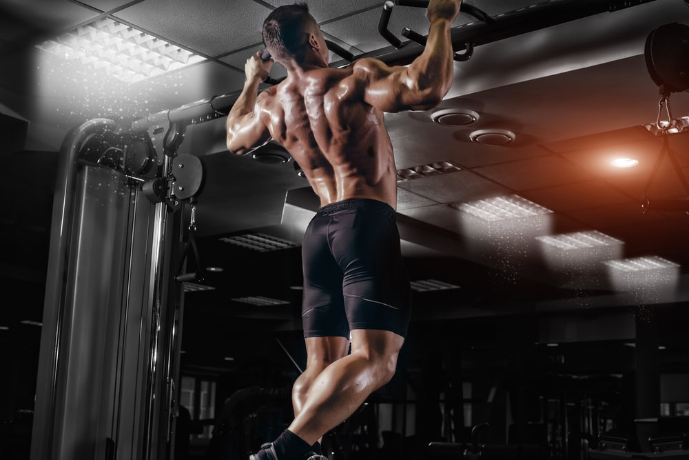 power muscular bodybuilder guy doing pullups in gym